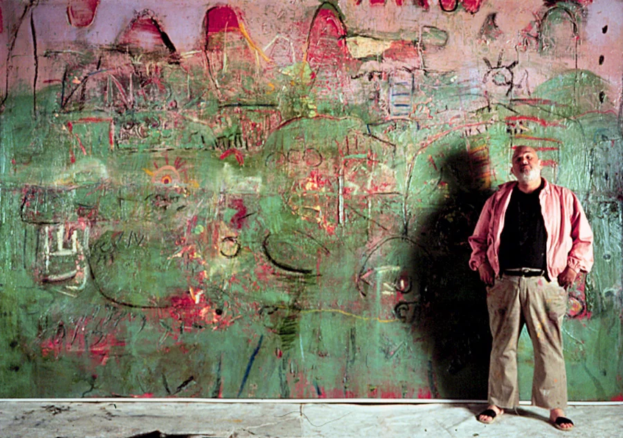 Layne Meacham standing in front of a wall-sized green and pink abstract painting in his studio
